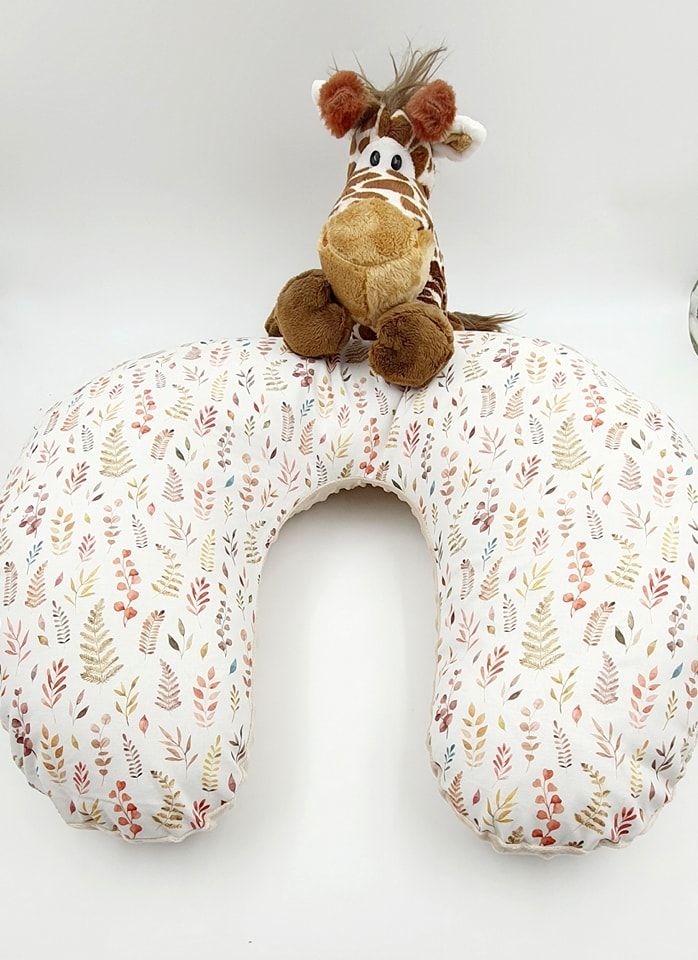 White nursing pillow with delicate floral pattern and small plush animal decoration.
