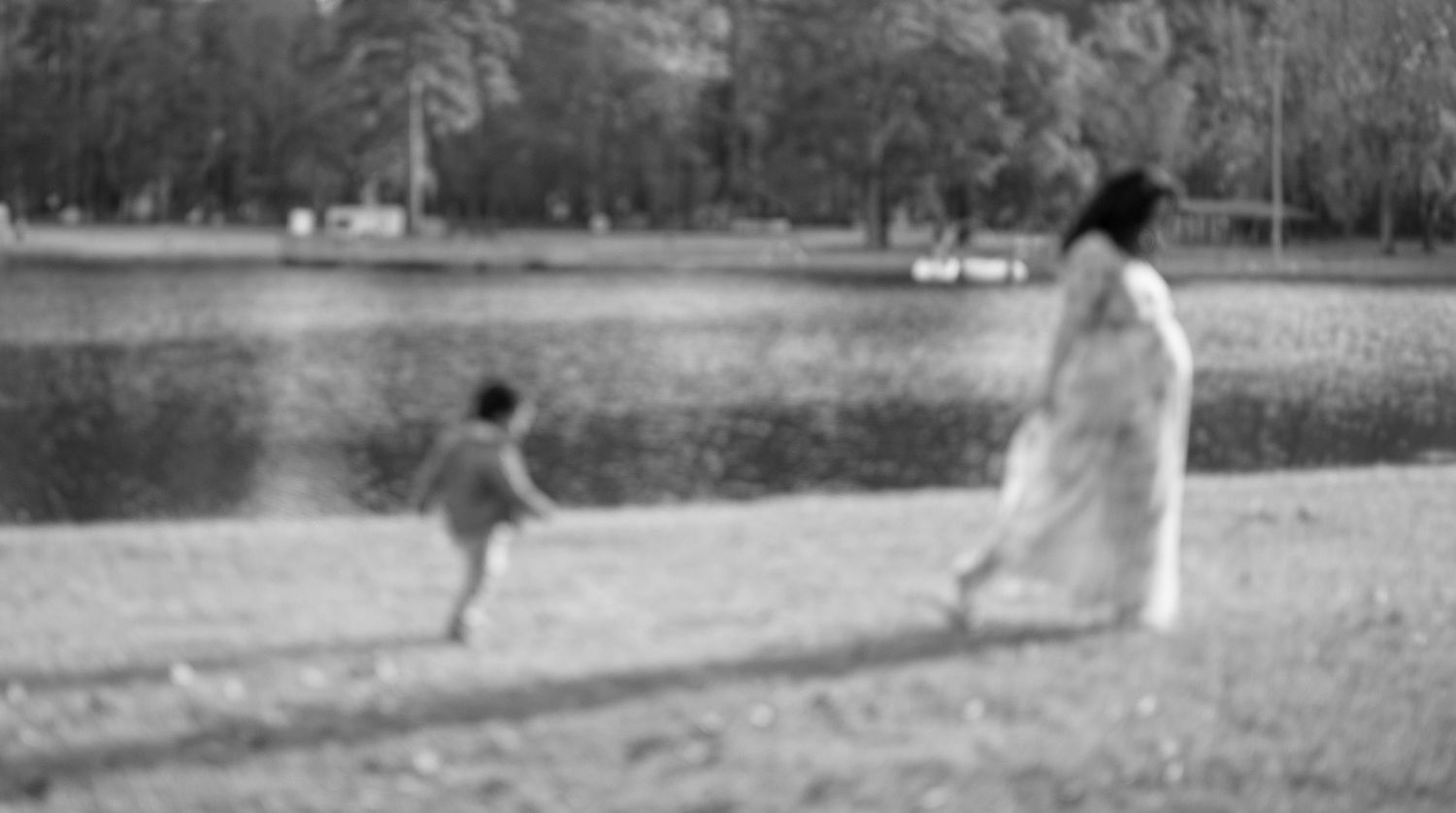 Black and white photo of two figures walking near a lake on a sunny day.