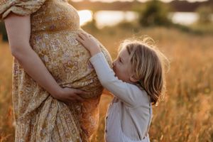 A big brother kissing his mums pregnant belly during a relaxed and beautiful outdoor family photoshoot at sunset by India Foxx photography