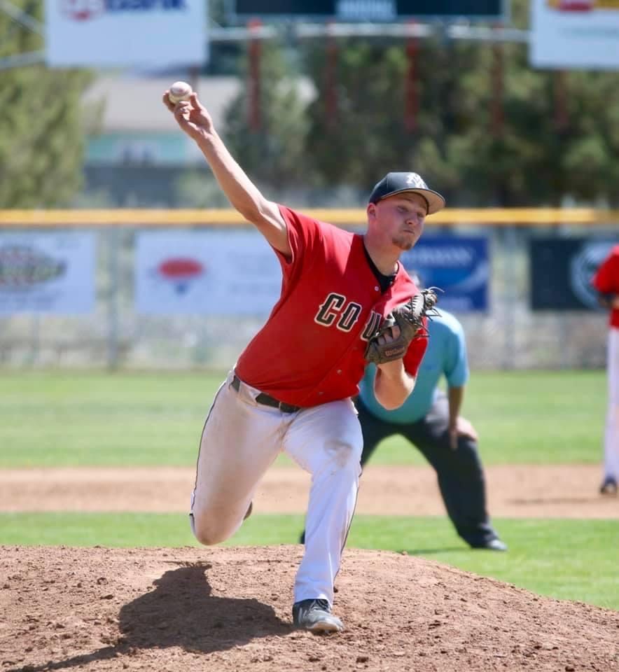 Baseball pitcher in red uniform mid-delivery on the mound during sunny game.
