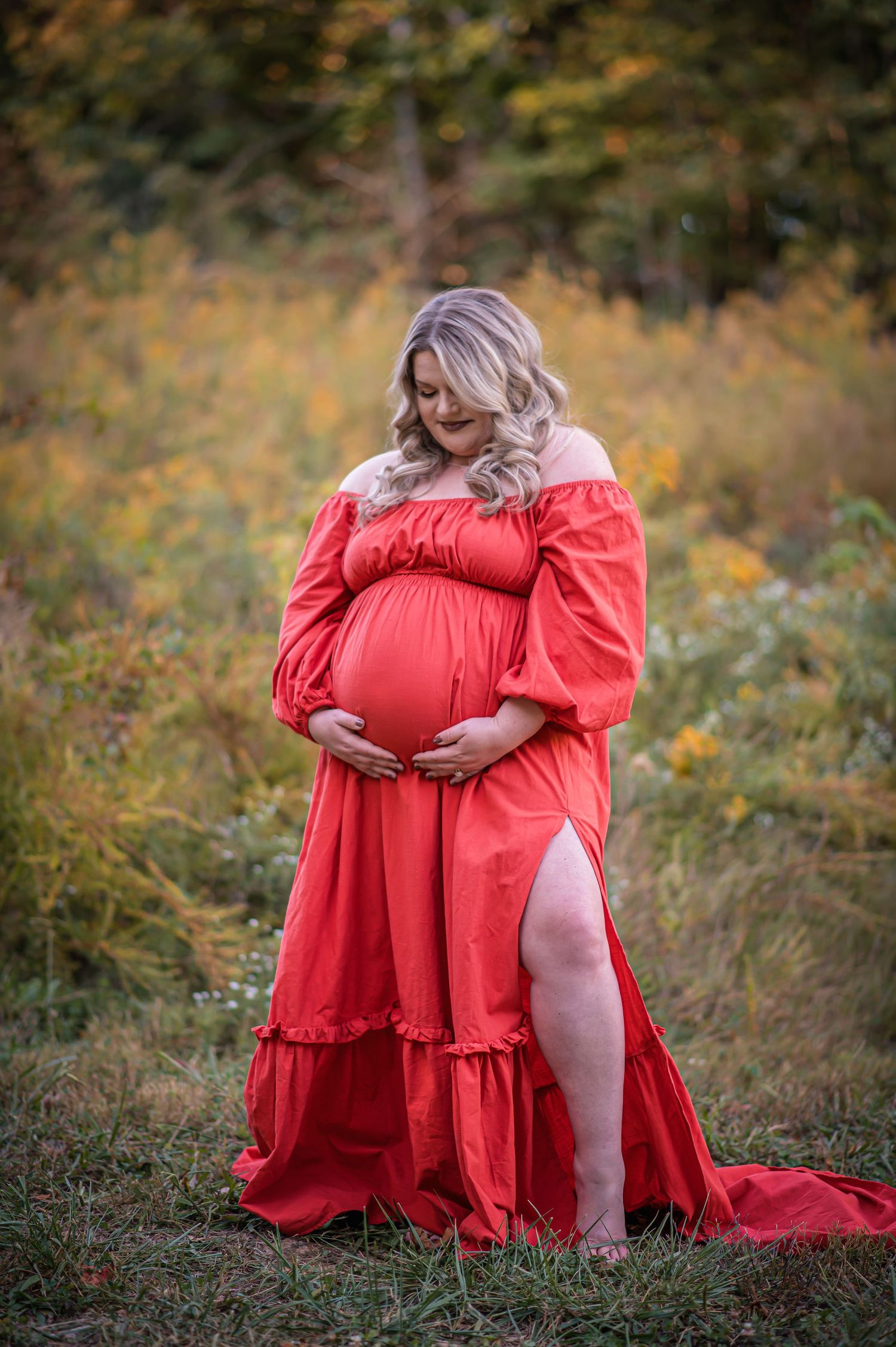 Romantic maternity portrait in coral dress with slit amid autumn grass.