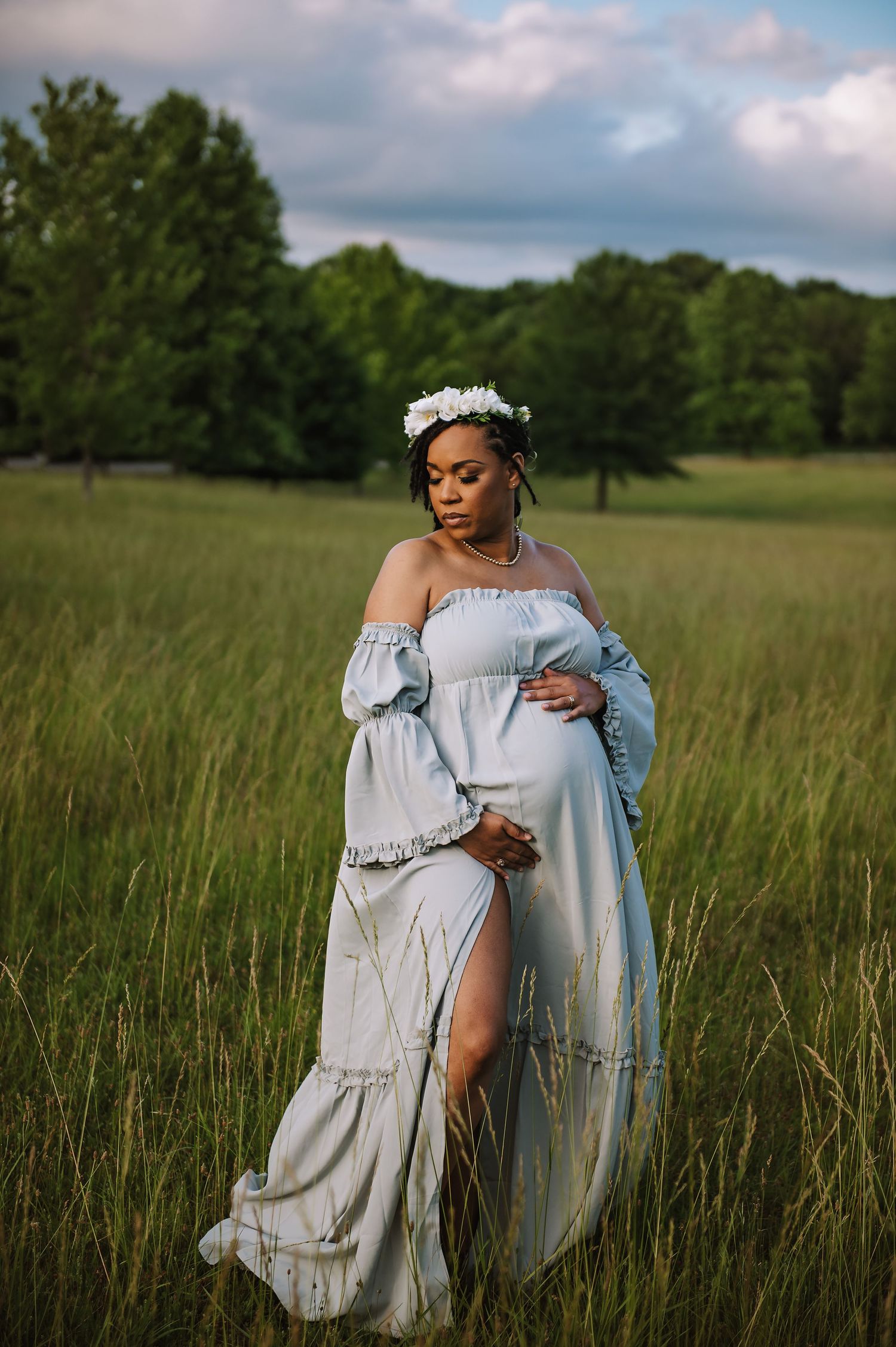 Ethereal maternity portrait in flowing white dress standing in golden meadow.