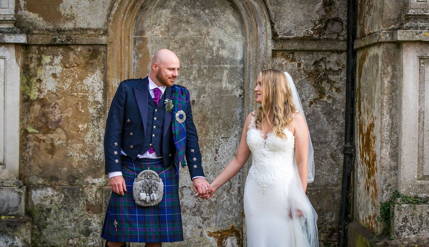 Wedding couple poses against weathered stone castle walls and archways.
