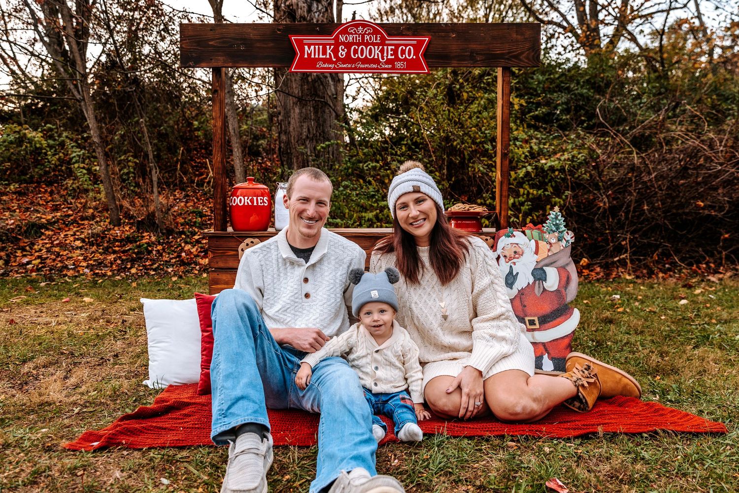 Family holiday photo with red truck backdrop and Christmas decorations outdoors.