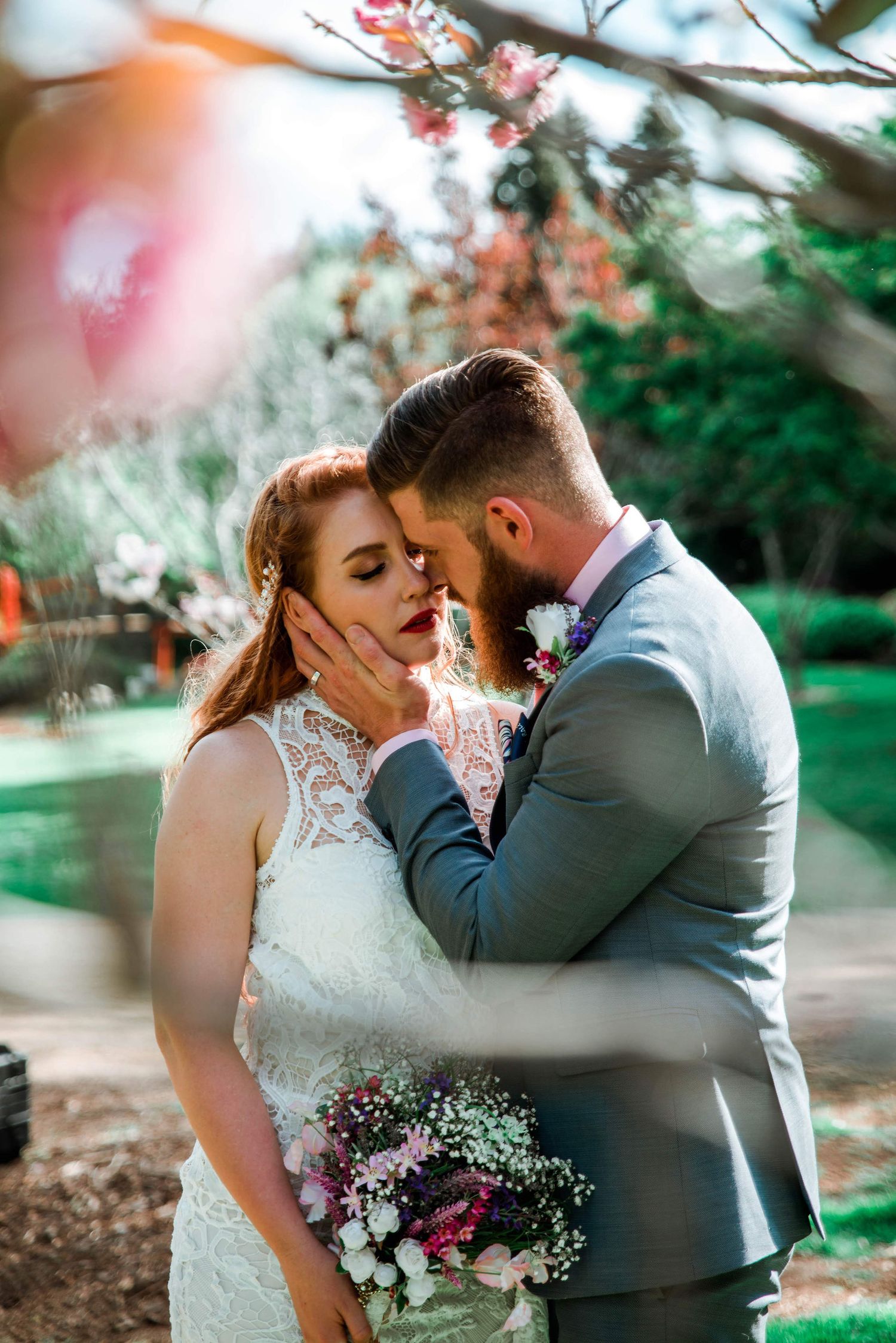 Intimate garden wedding portrait with blooming trees and wildflower bouquet.