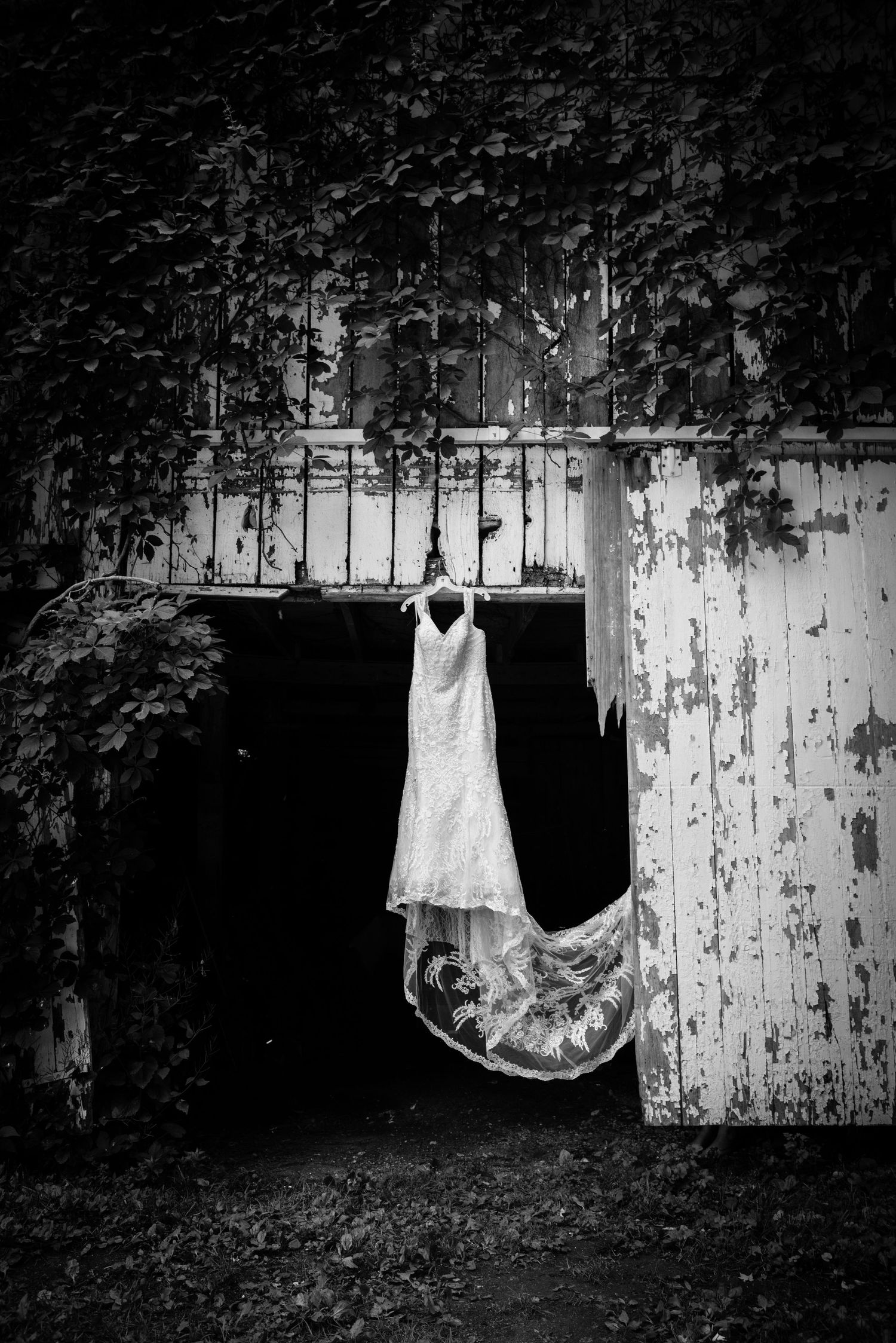 Artistic black and white series of vintage white dresses hanging against weathered wall.