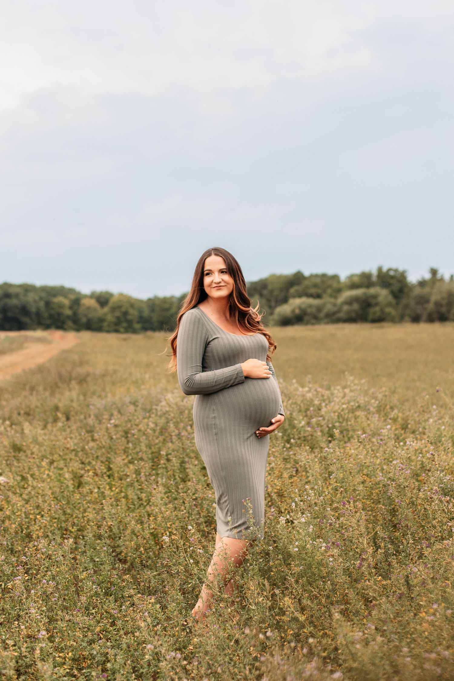 Maternity lifestyle portrait photography session for an expecting mother in a green field at sunset