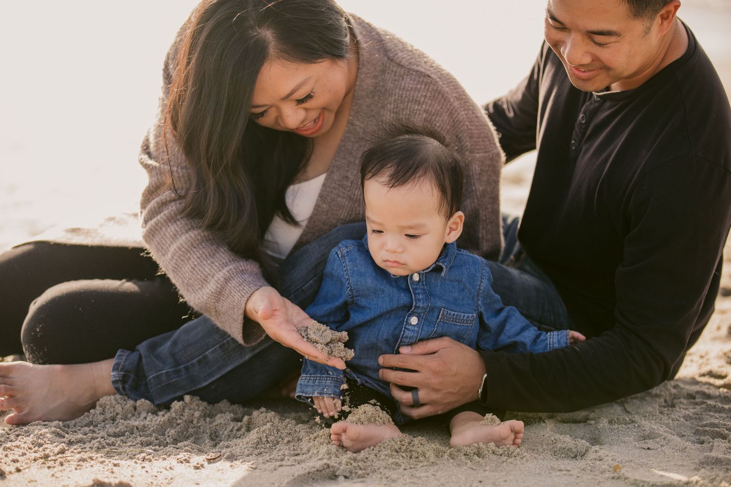 A tender family moment on the beach with parents and baby playing in the sand.