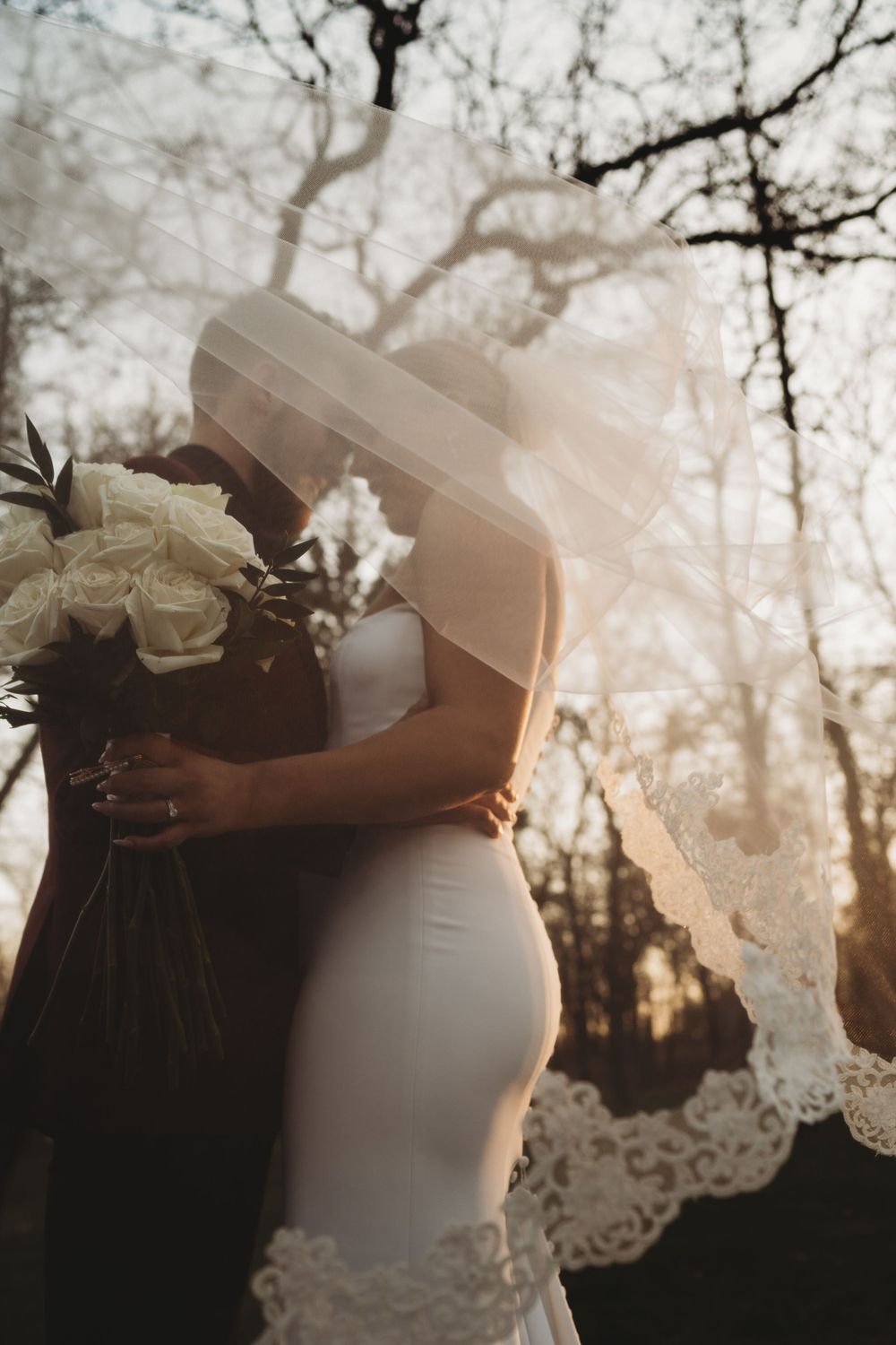 Artistic silhouette of a bride holding flowers with sunlight filtering through lace veil.