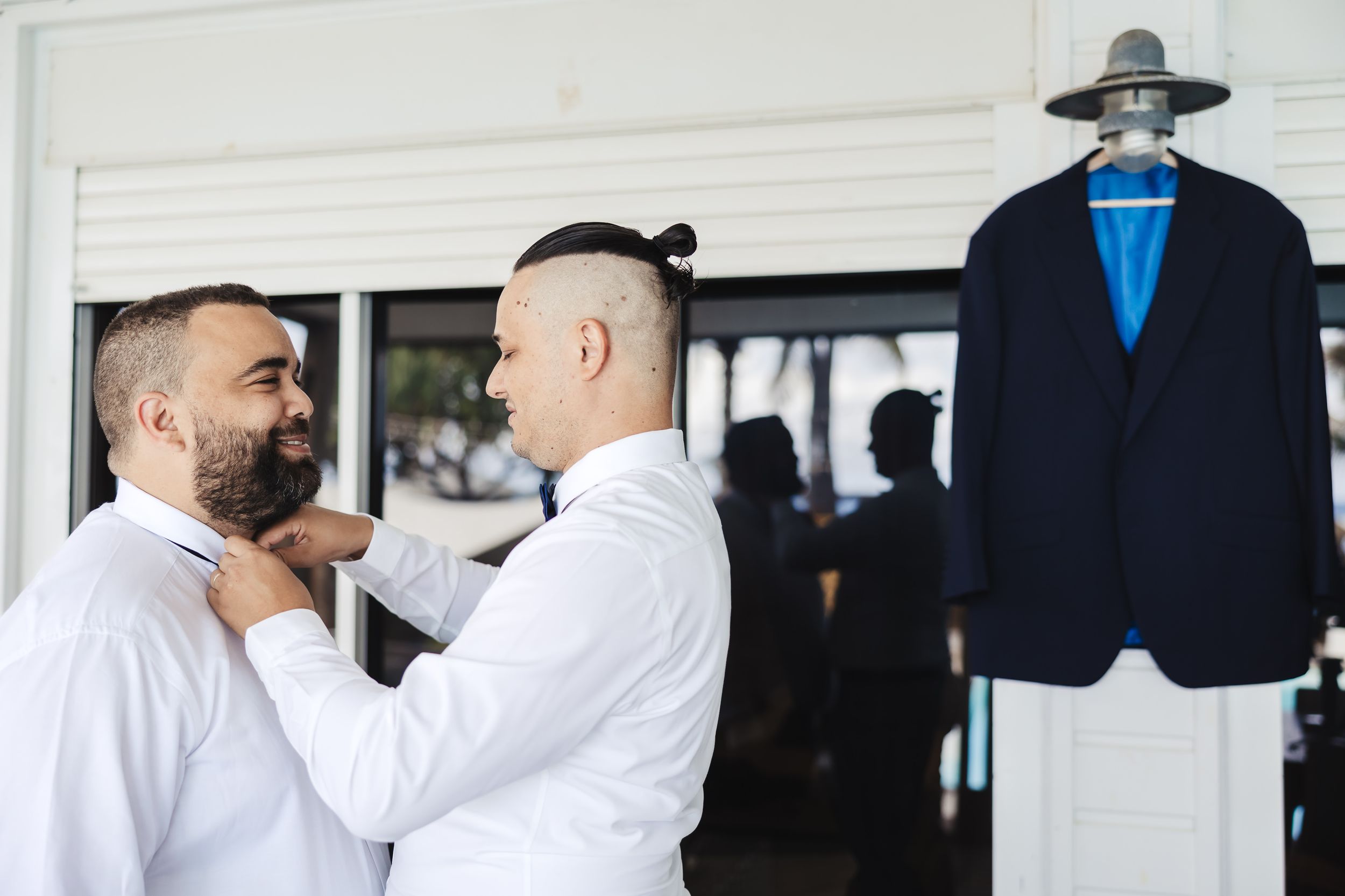 Men in formal attire adjusting suits and getting dressed in a dressing room.