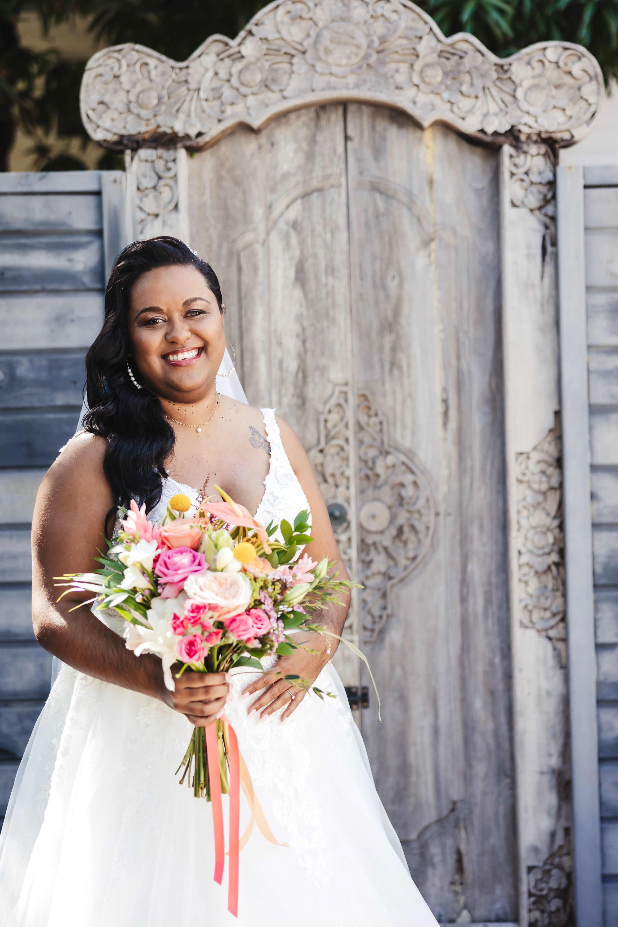 Bride in white dress holding colorful bouquet against ornate stone backdrop.