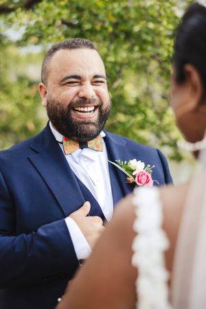Close-up shots of groom in navy suit with wooden bow tie and pink boutonniere.