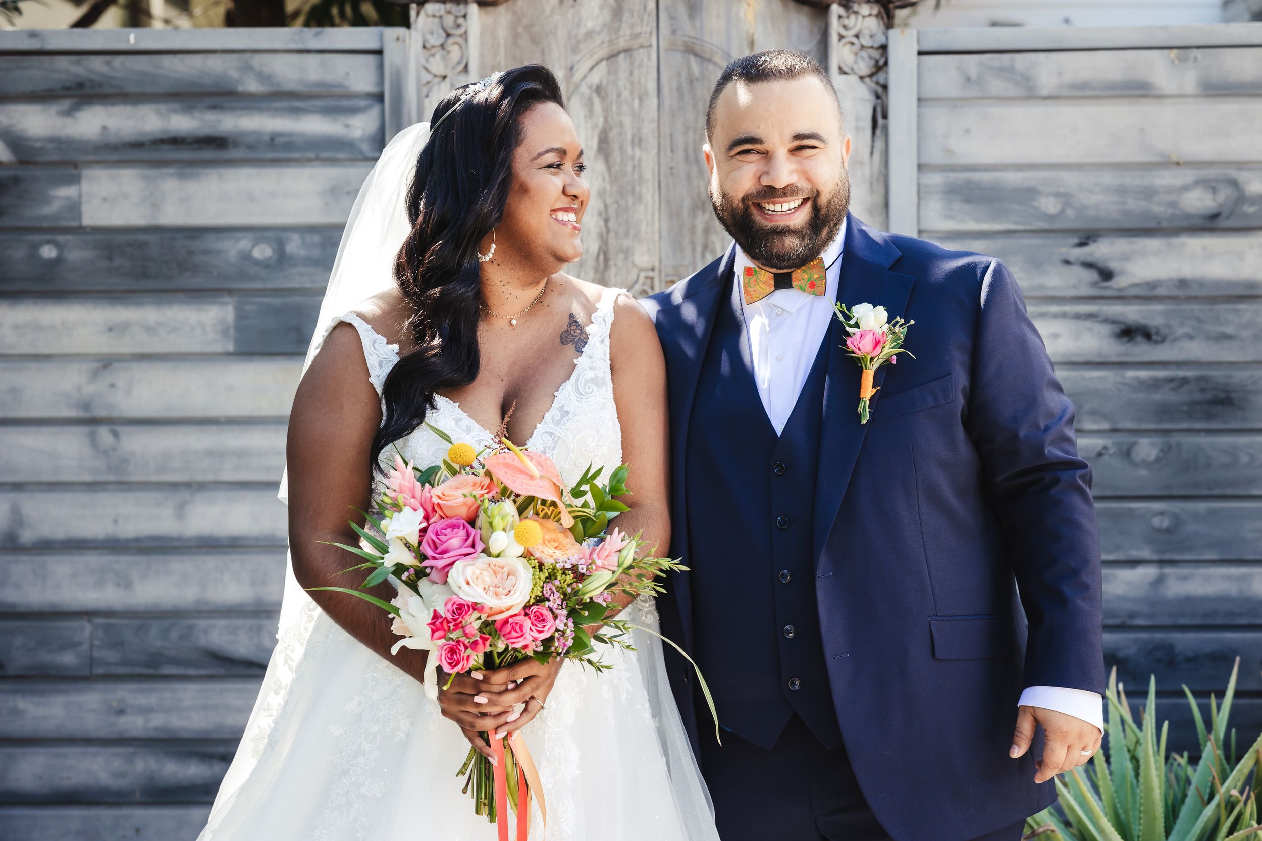 Wedding couple posing together outdoors with colorful floral bouquet.