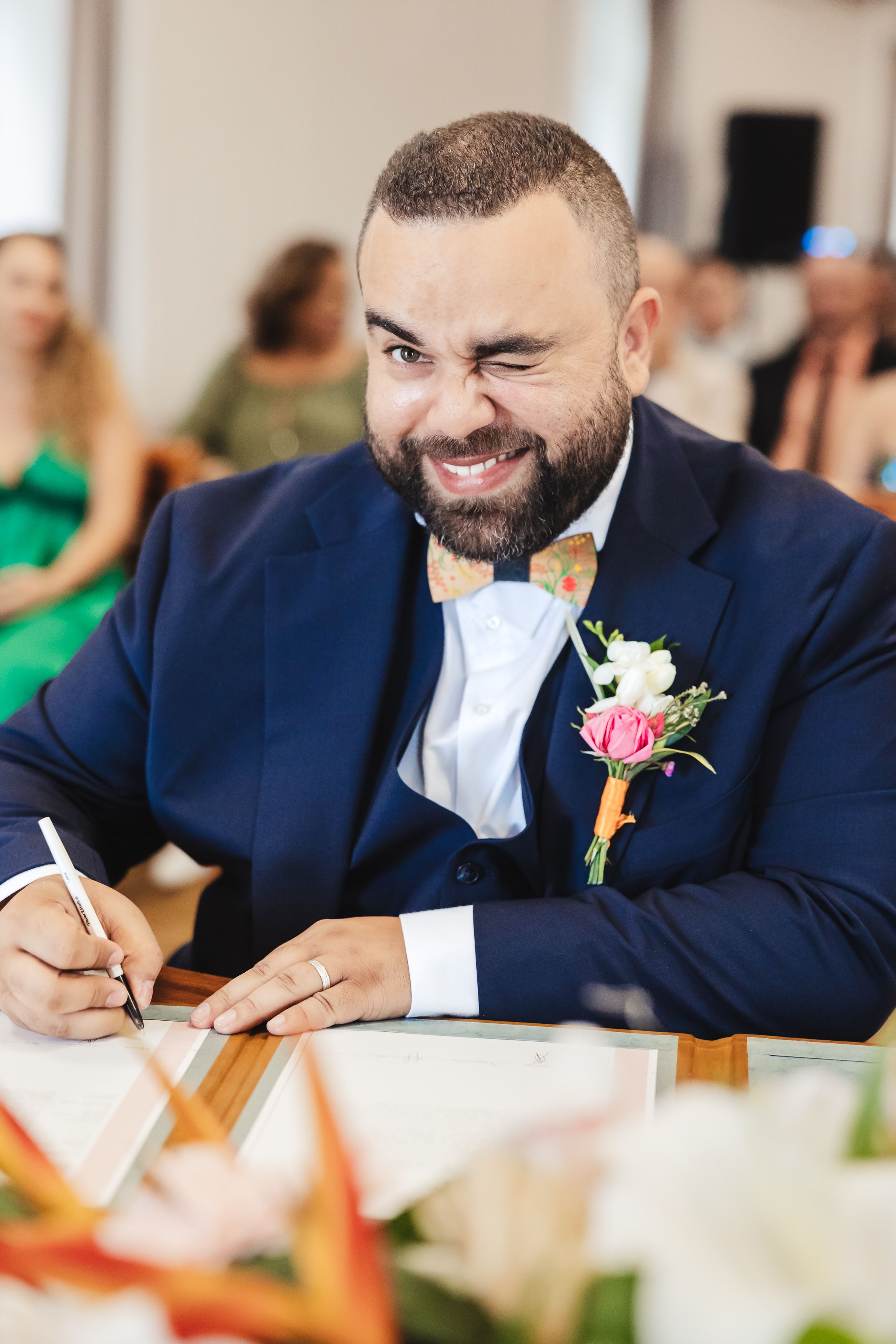 Groom in navy suit with floral boutonniere smiles joyfully during wedding reception.