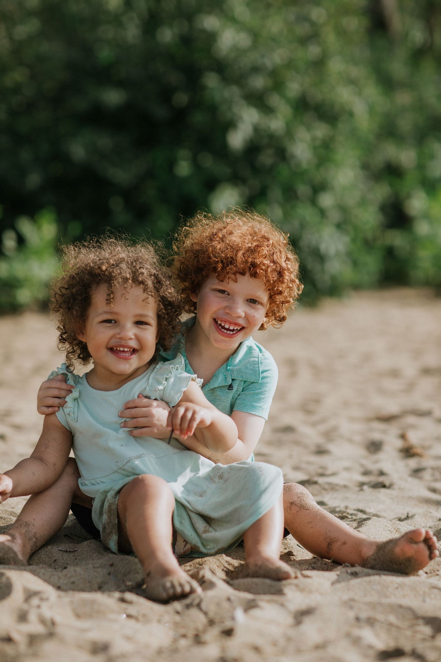 Two children in matching mint outfits playing together on sandy beach.