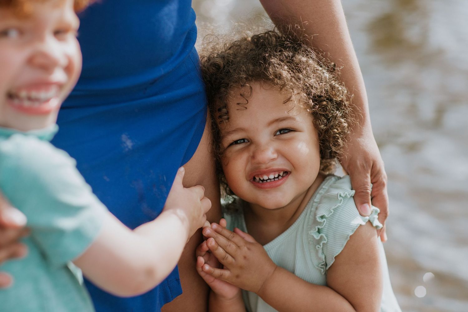 Child in light blue outfit enjoys playful moment at water's edge.