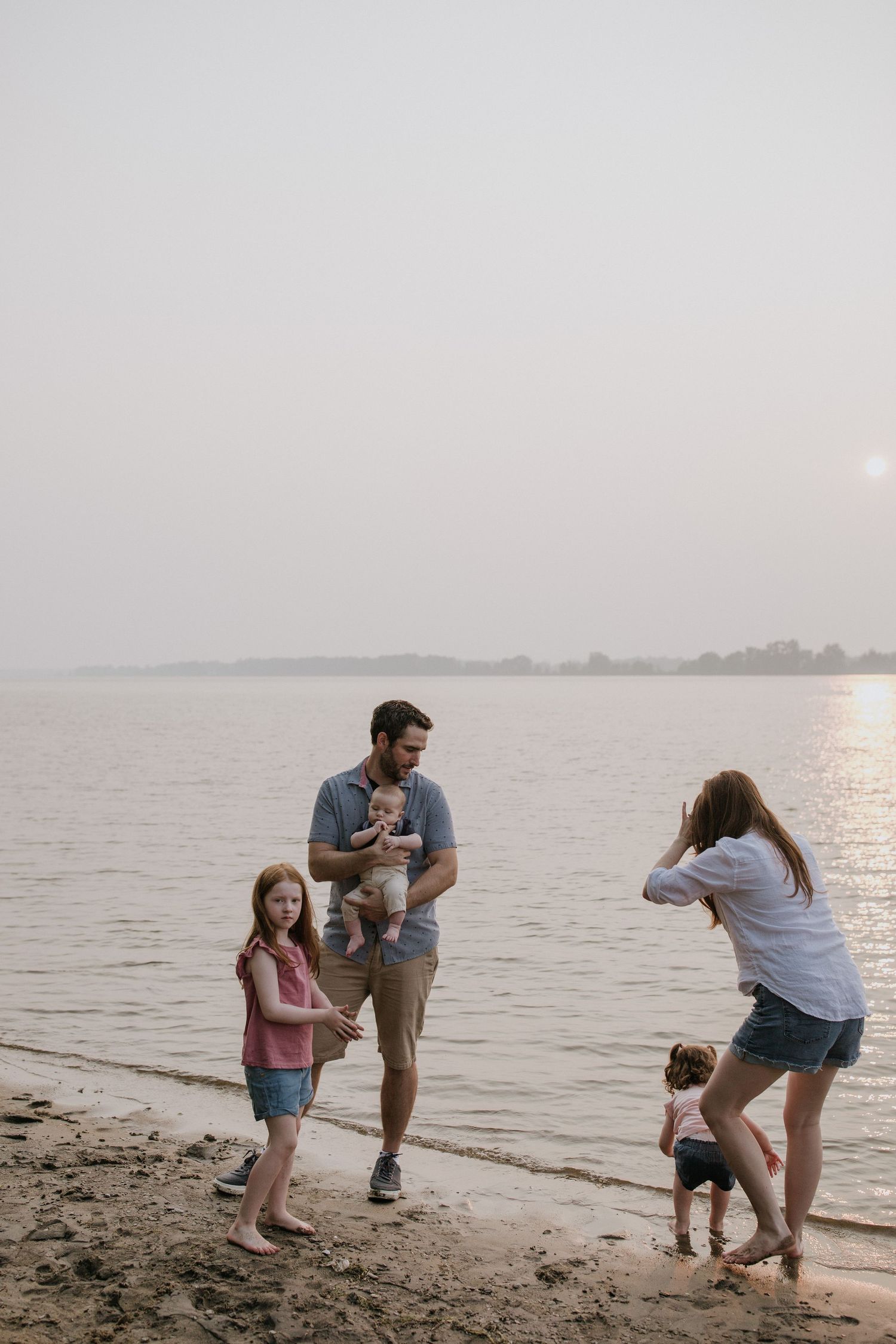 Family enjoying playful moments together on a misty beach at sunset.