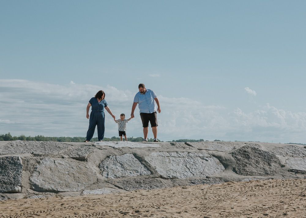 Family silhouettes standing together on rocky beach terrain against blue sky.
