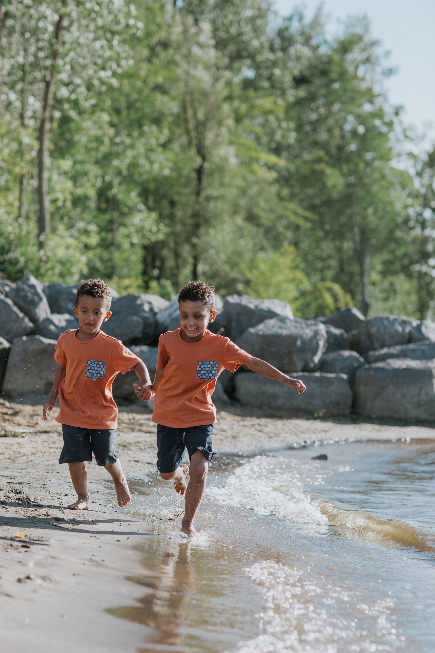 Children in orange shirts splashing and playing in beach water.