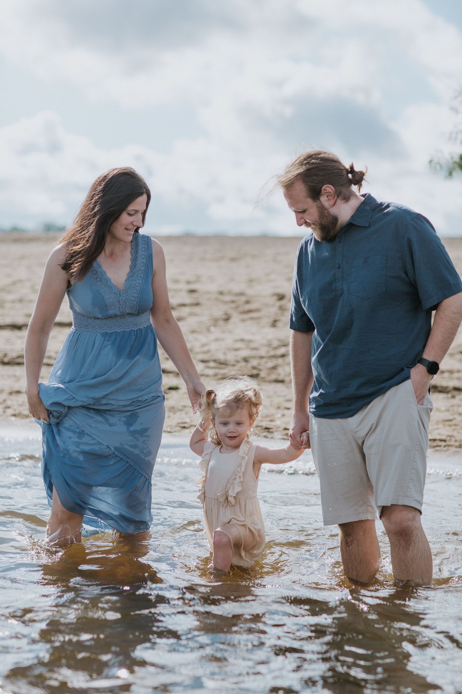 Family wading together in shallow water at beach during summer day.