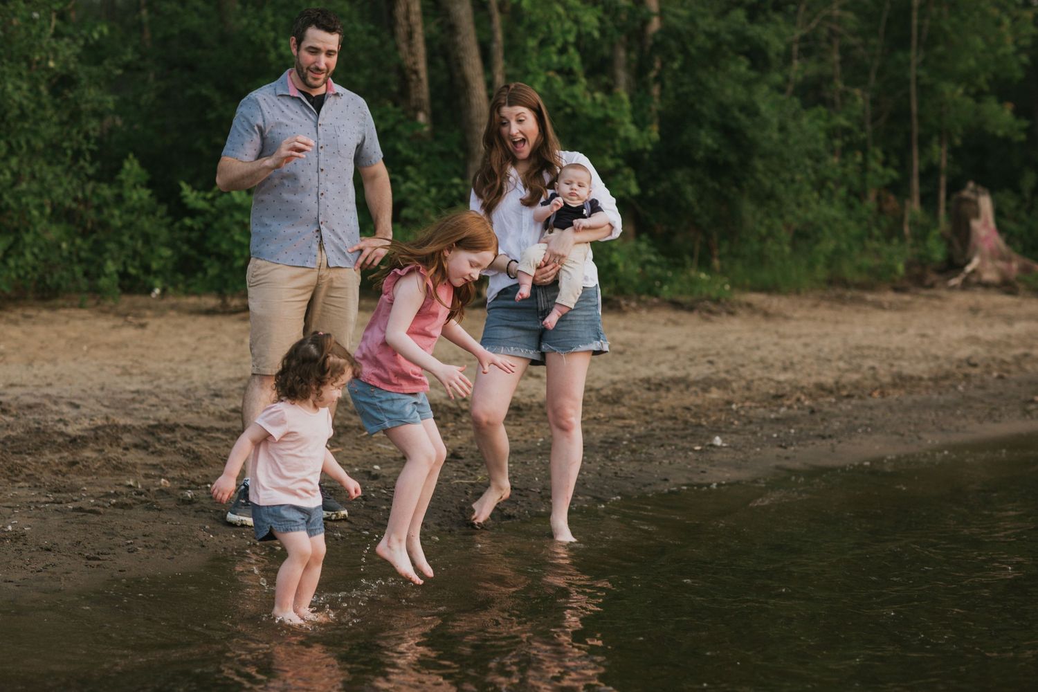 Family playing together at the water's edge of a wooded lake.