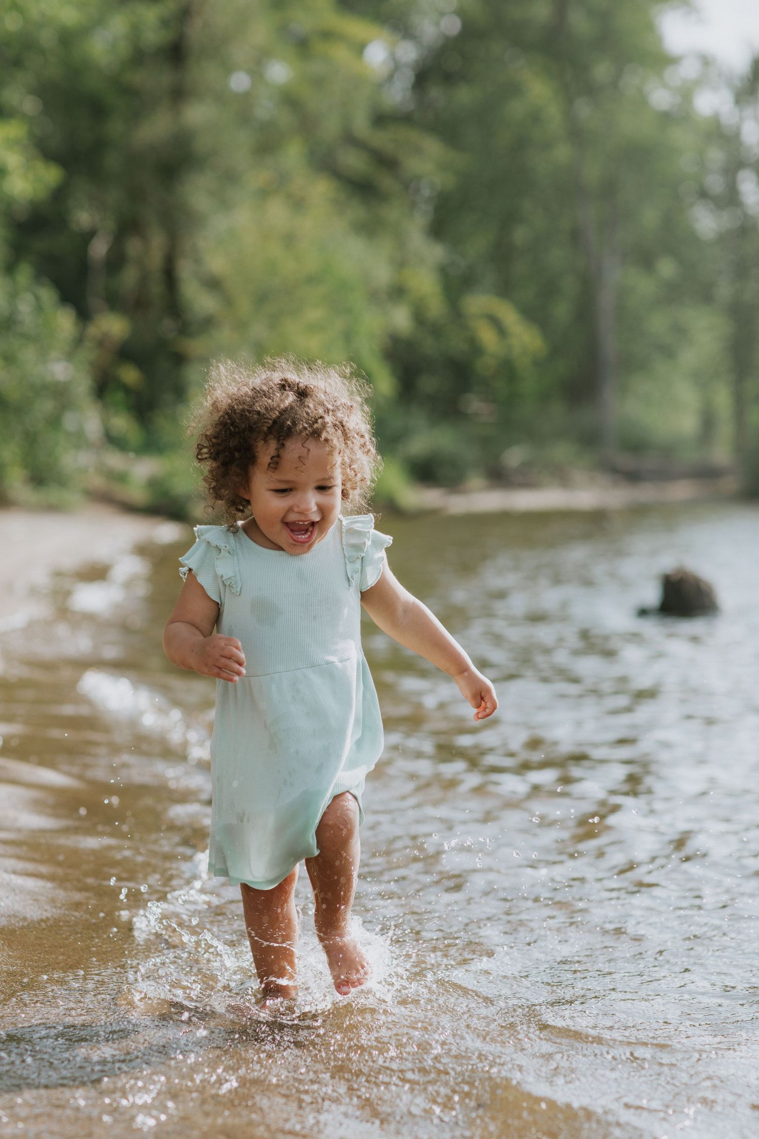 Toddler in mint green outfit splashing happily in shallow water.