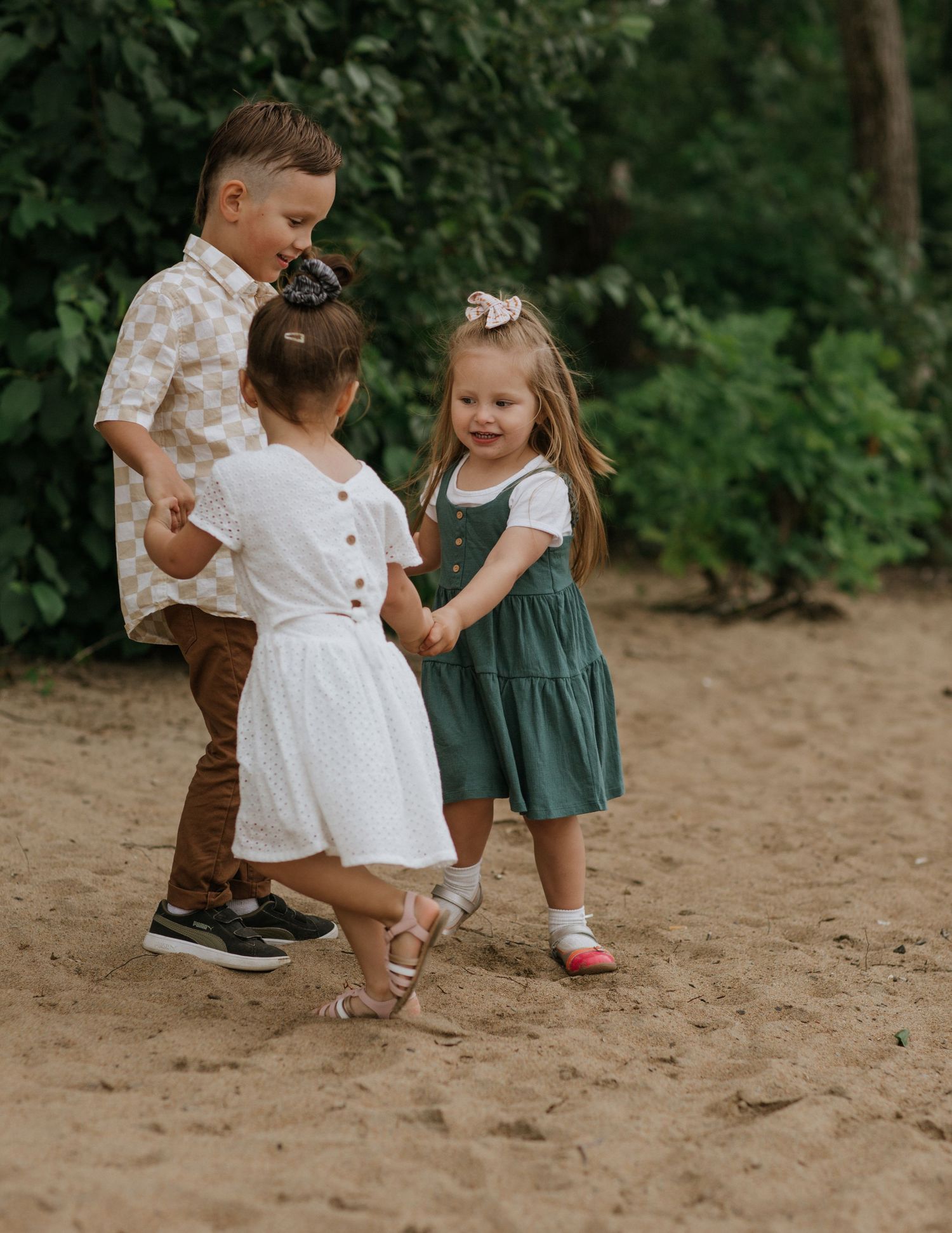 Children playing together on a sandy path surrounded by green foliage.