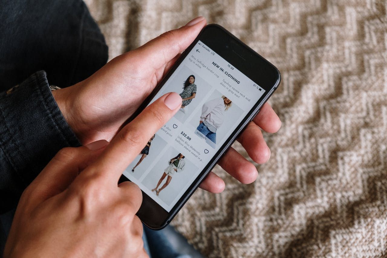 Hands holding smartphone displaying online shopping interface with clothing items.