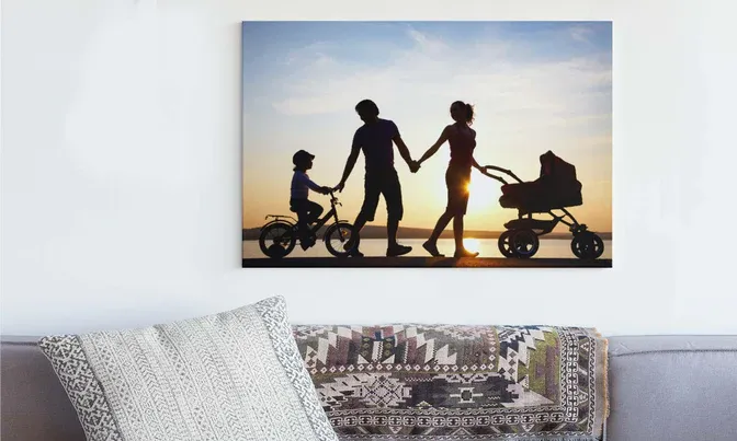 Silhouette canvas print of family walking at sunset displayed above grey couch.