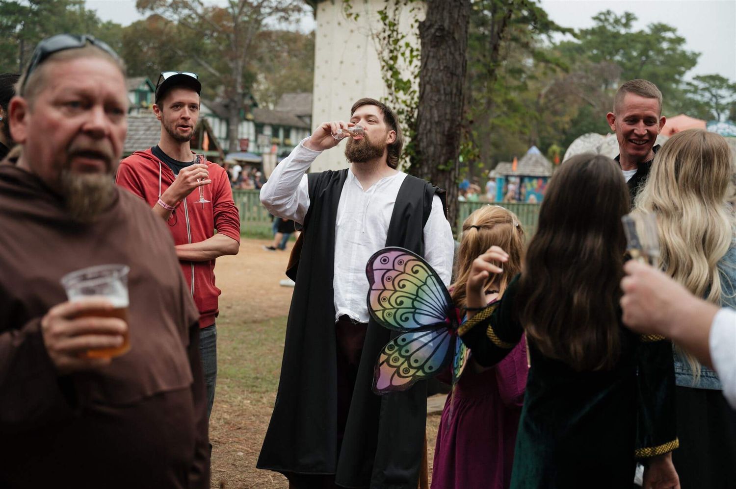 Group gathered at an outdoor renaissance festival with costumes and drinks.