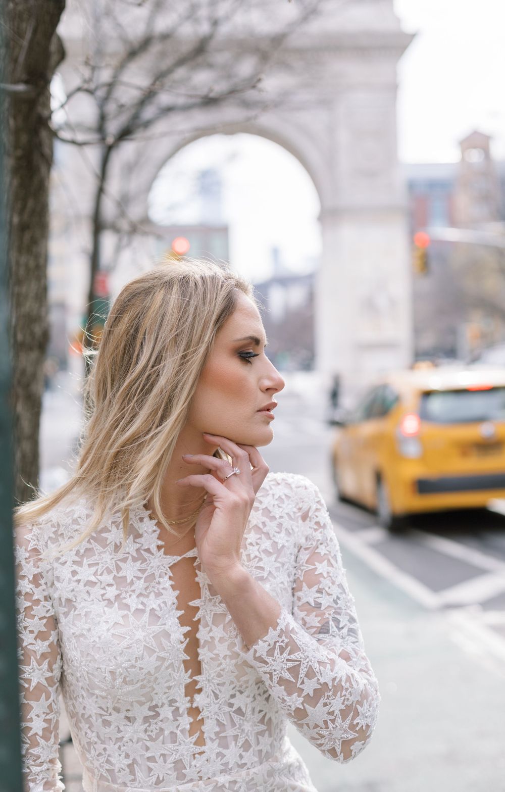 Elegant lace wedding dress with plunging neckline photographed in front of Washington Square Arch with yellow taxi in background.