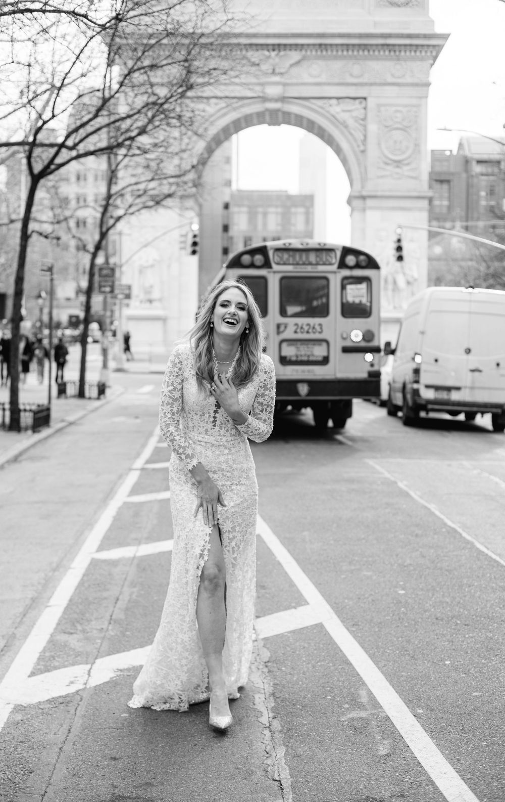 Urban bridal portrait with lace jumpsuit against NYC streetscape and arch backdrop.