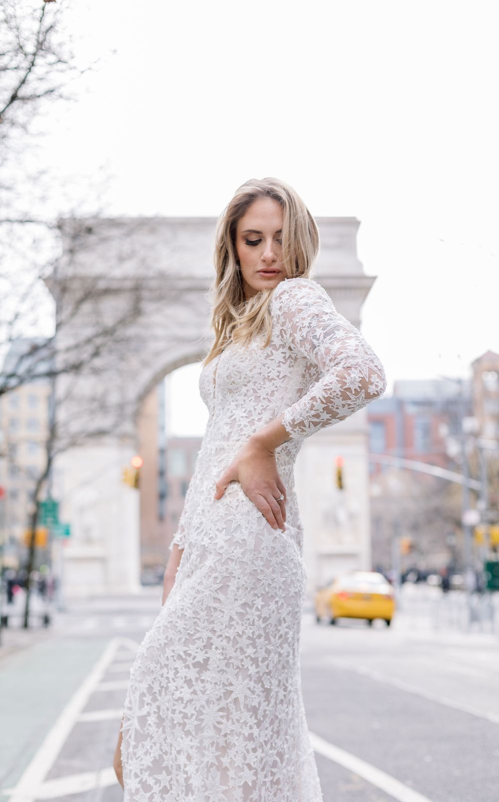 Side profile of lace wedding gown against Washington Square Park arch and city street.