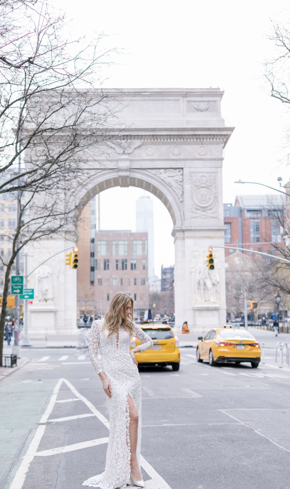 Long lace wedding dress photographed against Washington Square Arch with yellow taxis in frame.