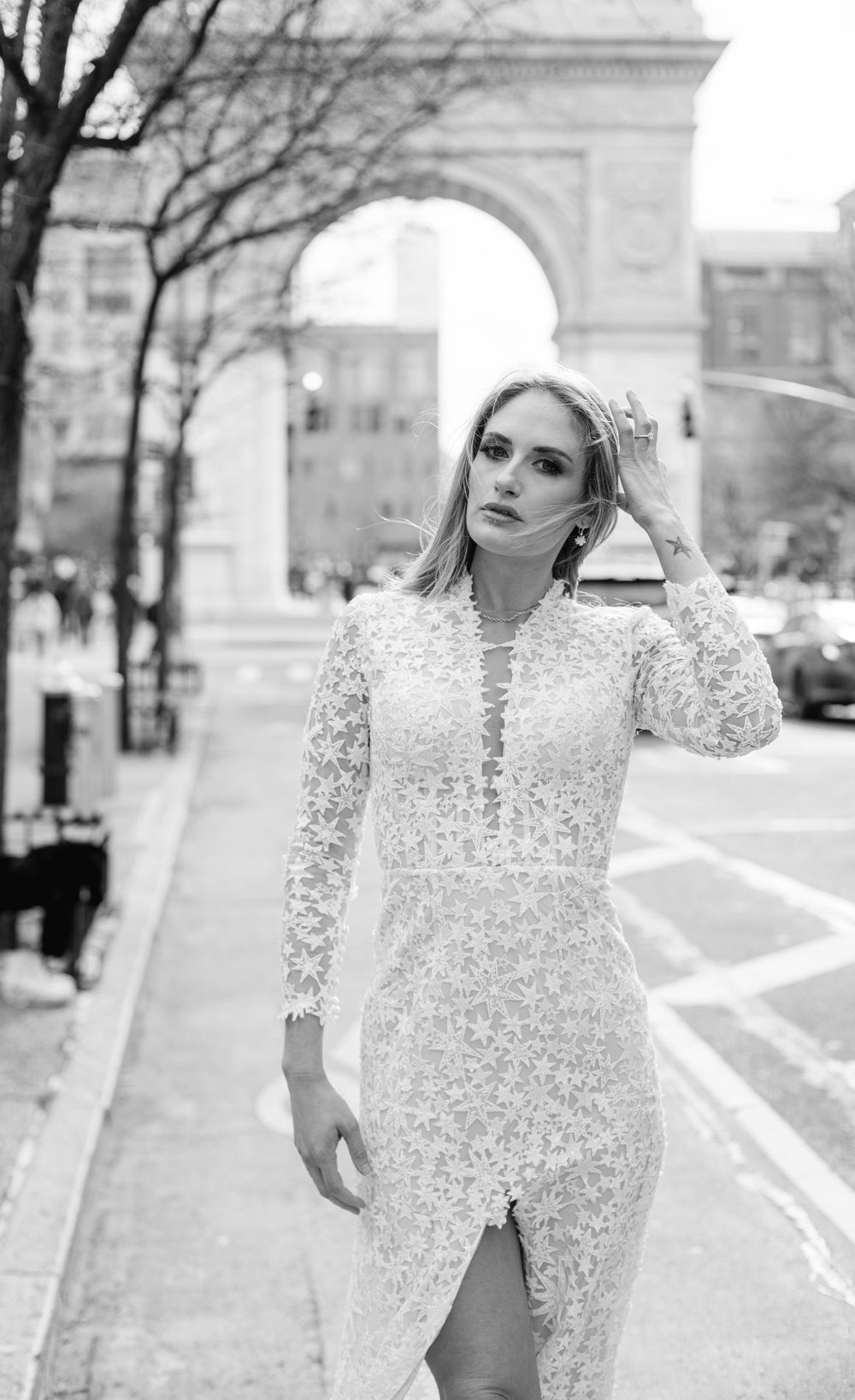 Black and white portrait of bride wearing fitted lace gown with slit in front of historic arch monument.