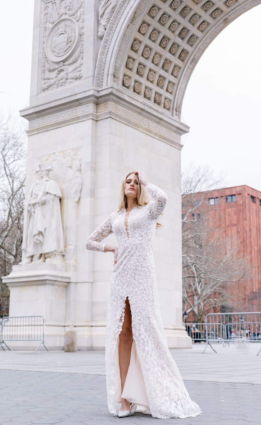 Full length white lace bridal gown with slit posed against historic arch architecture.