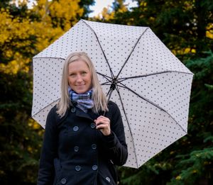 Person with polka dot umbrella smiling against autumn foliage background.