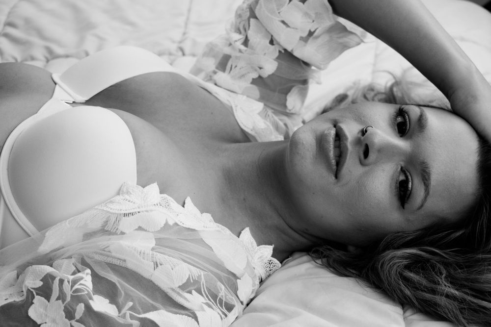 Black and white boudoir photo with soft lighting and white fabric elements.