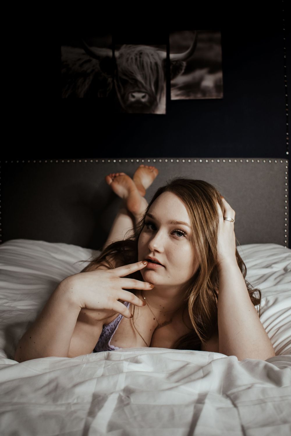 Person lying on white bedding in moody boudoir photography.