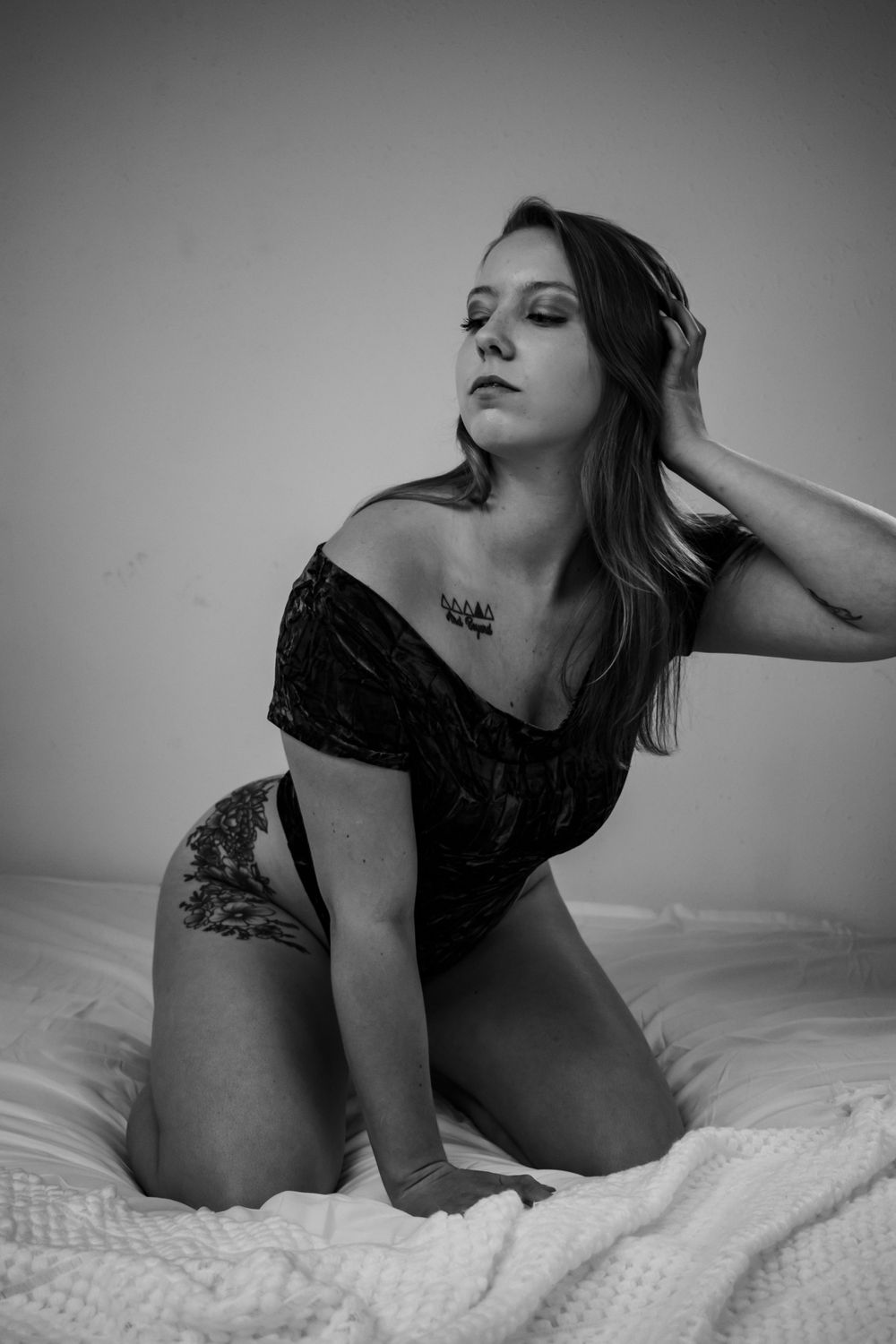 Black and white boudoir photo on textured bedding with dramatic shadows.