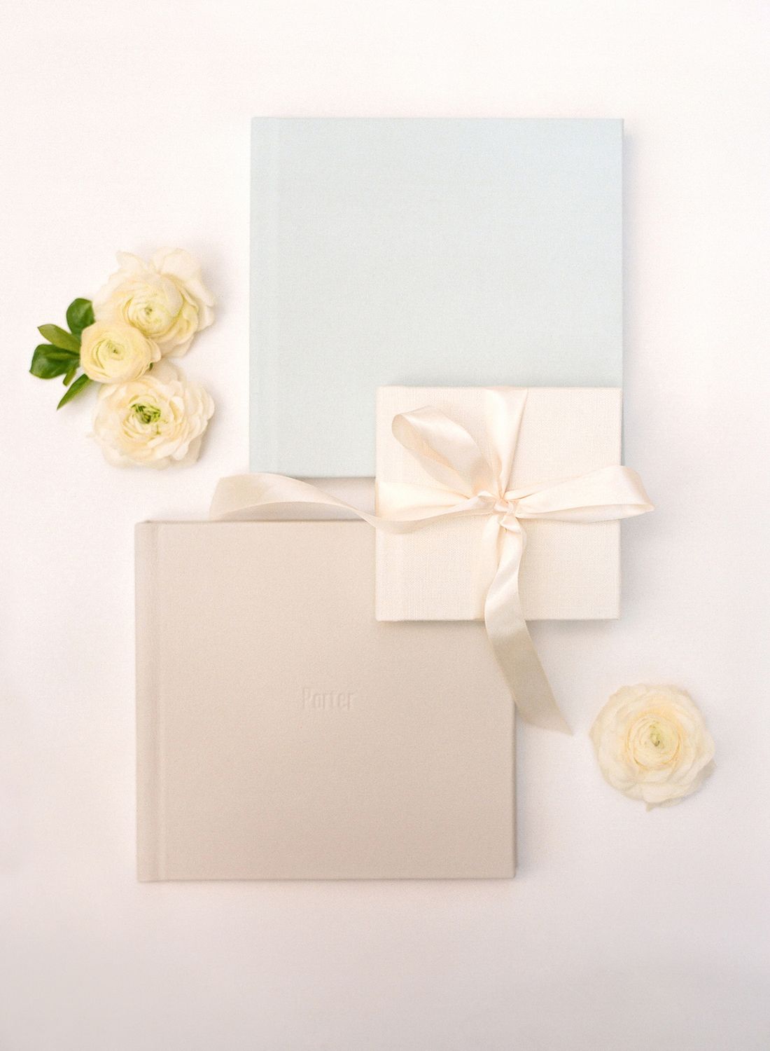 Wedding stationery flat lay with pale blue paper, cream box and white roses.