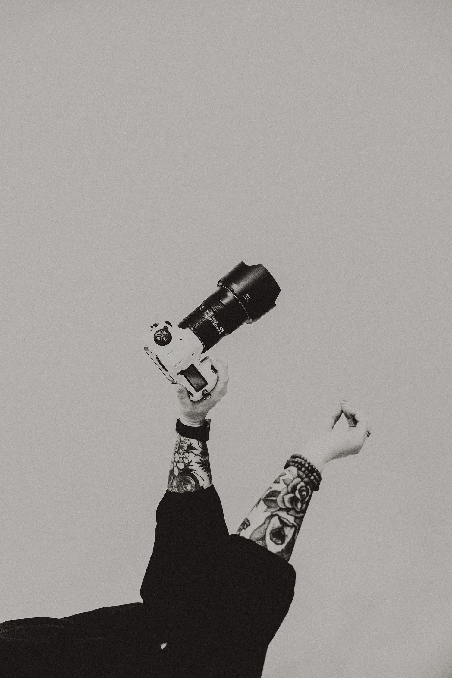 Tattooed hands holding professional camera against grey background.
