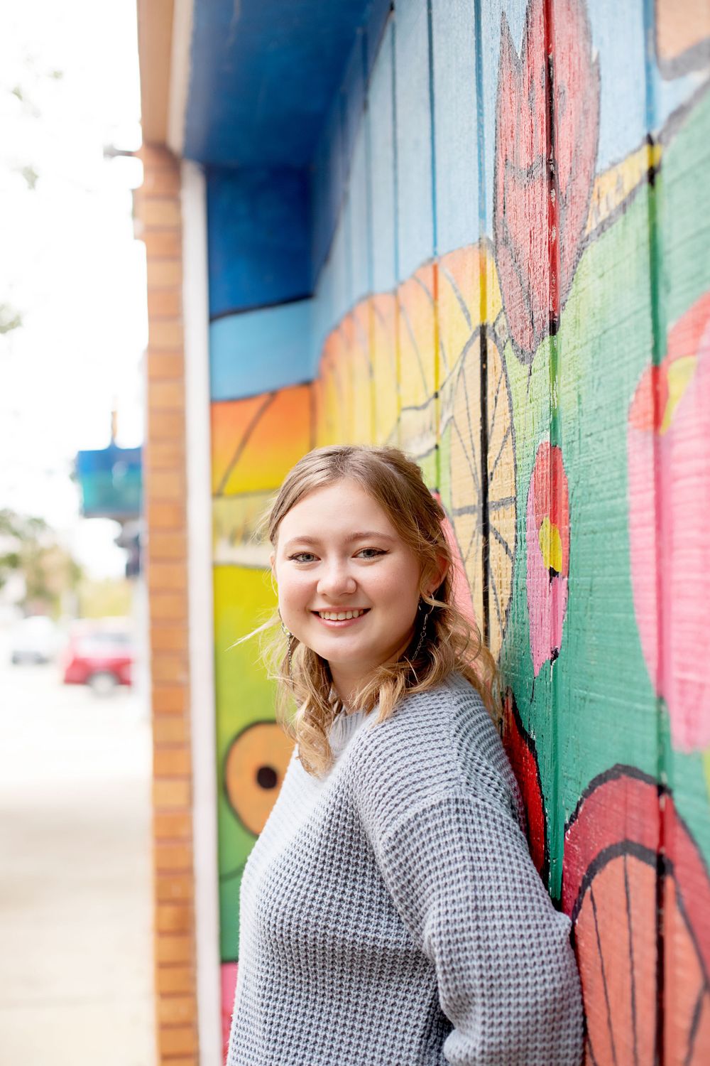 Person in chunky knit sweater poses by colorful outdoor mural.