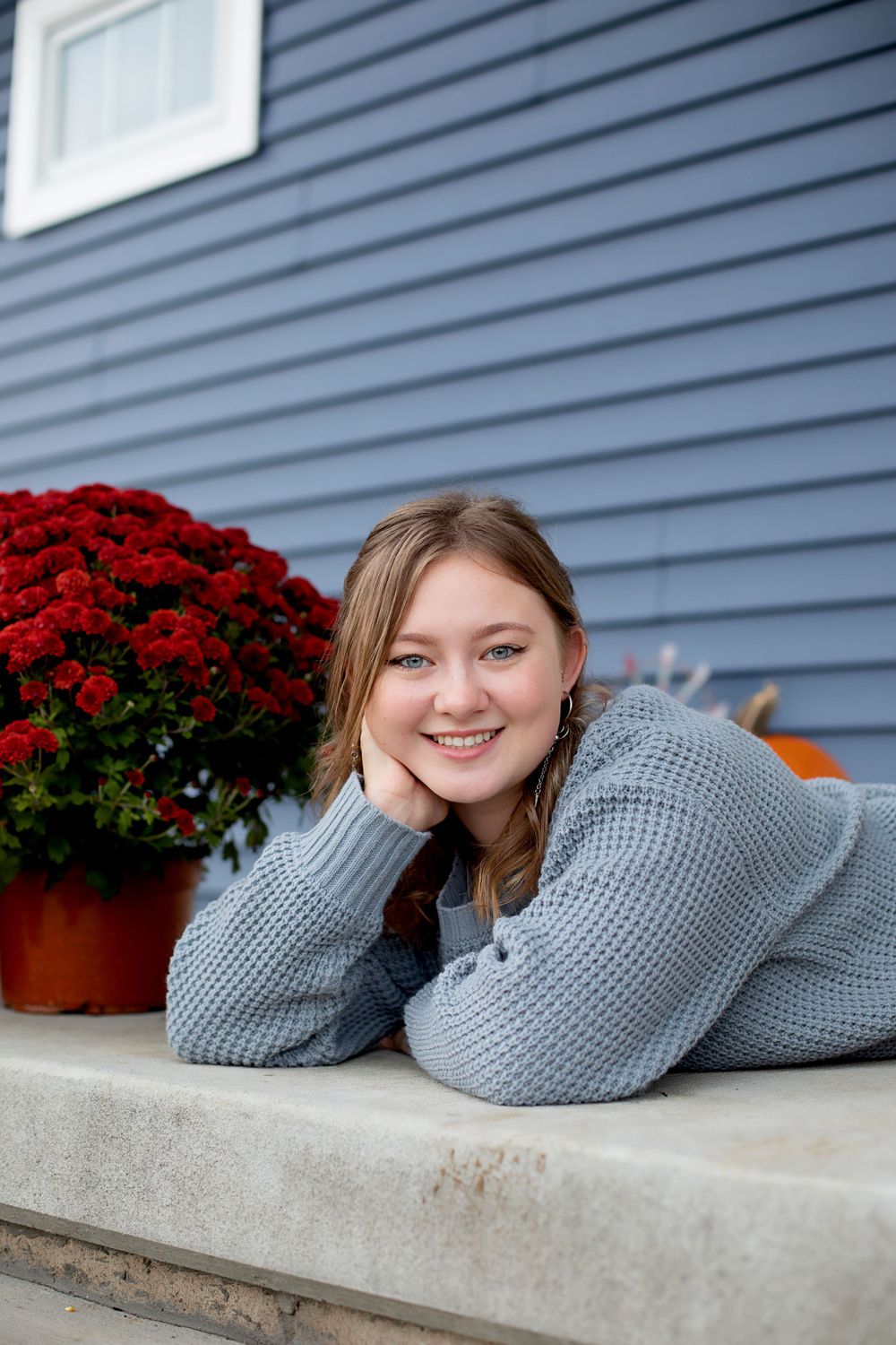 Casual portrait resting on concrete step with red flowers and blue siding in background.
