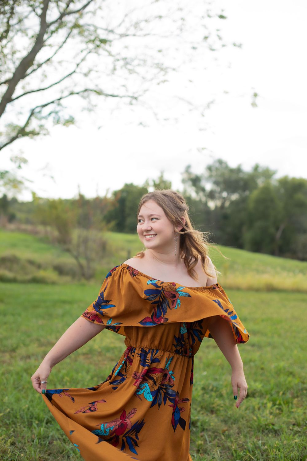 Dancing in a floral rust-colored dress in an open field during golden hour.