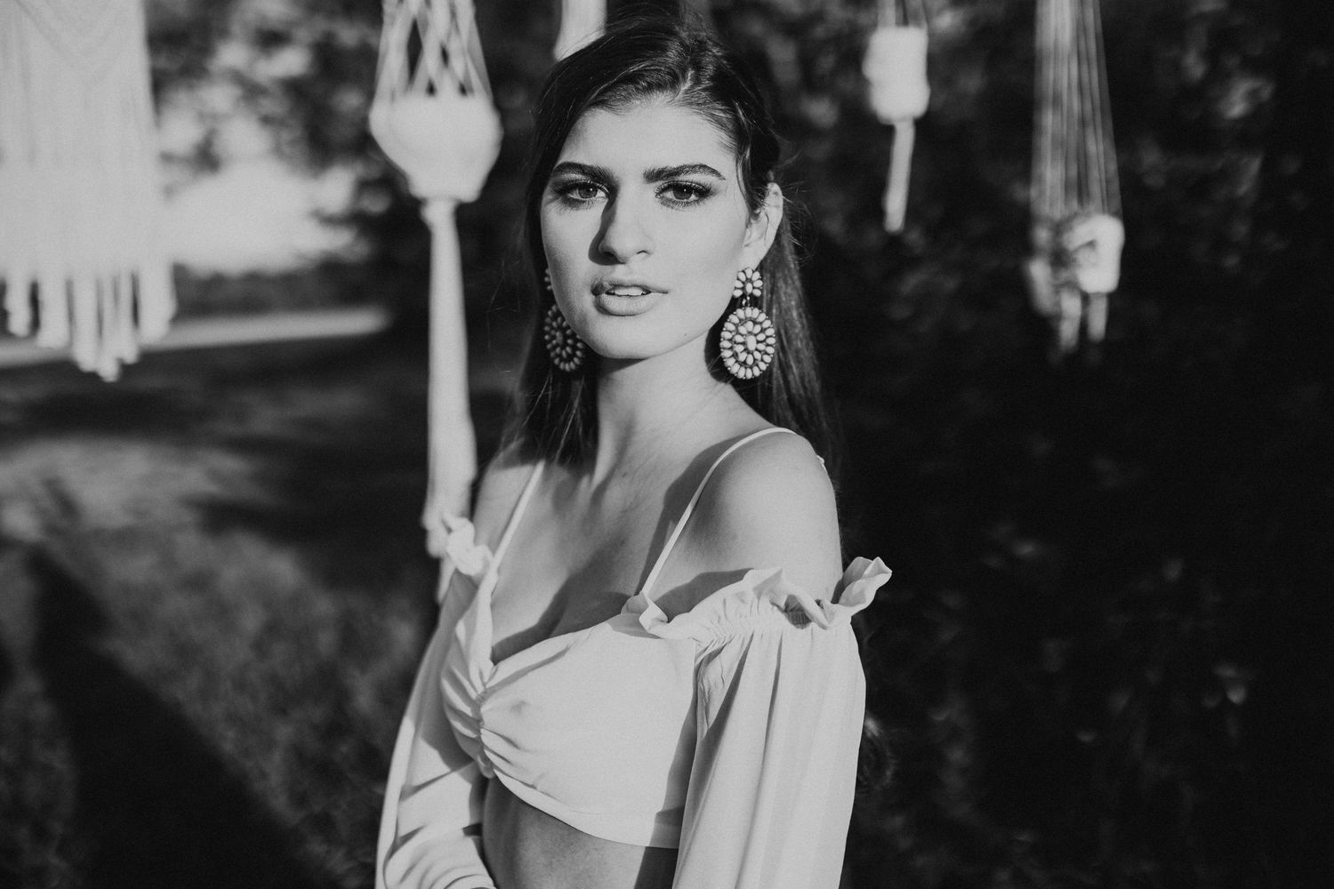 Black and white portrait of a woman in an off-shoulder dress and statement earrings in romantic outdoor lighting.
