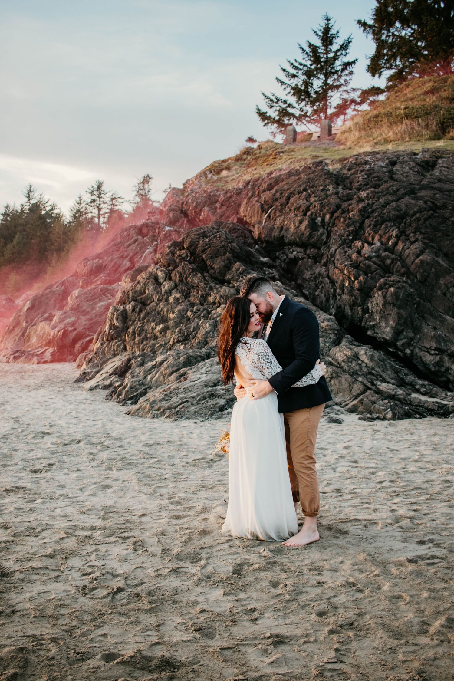Bride and groom standing infront of pink smoke during Tofino, British Columbia Beach Elopement