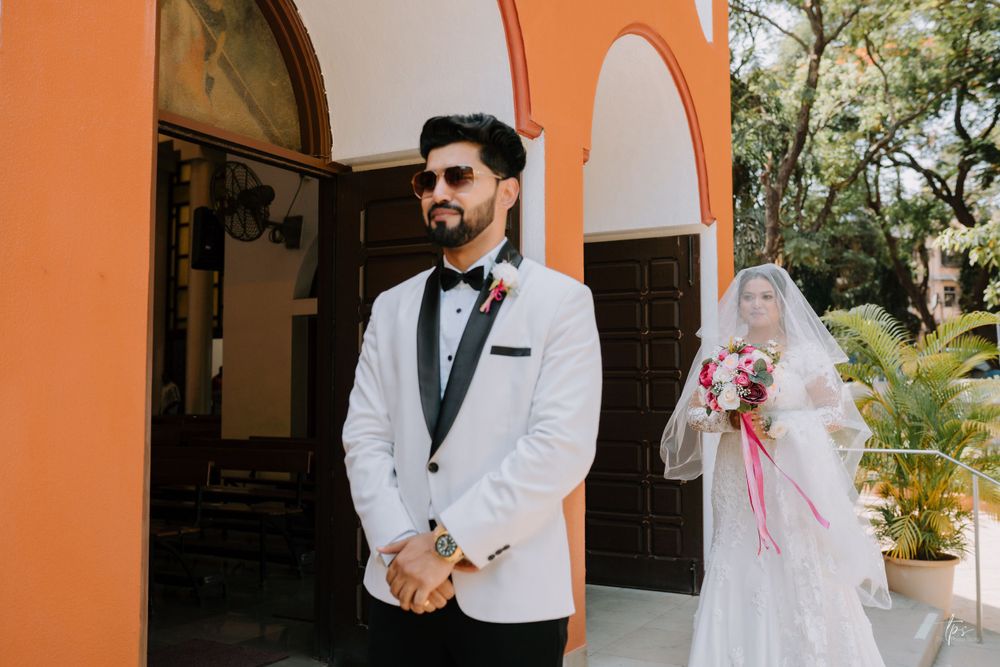 Wedding couple poses against orange wall in formal attire with floral accents.