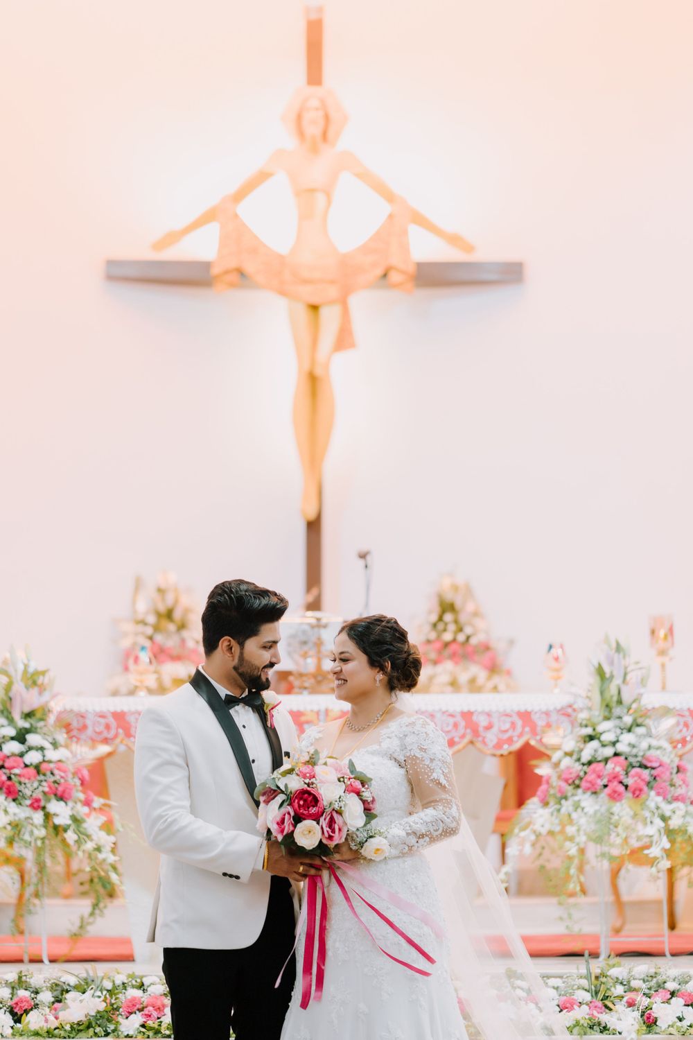 Couple poses for romantic wedding photos in front of floral decorations and cross.