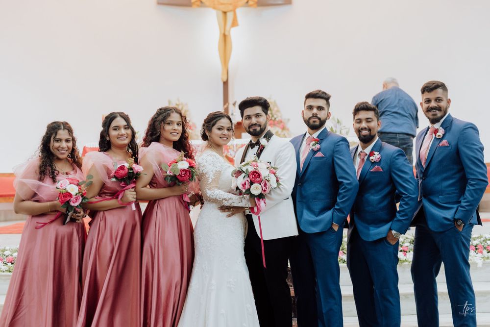 Wedding party in blue suits and pink dresses poses together for formal photos.